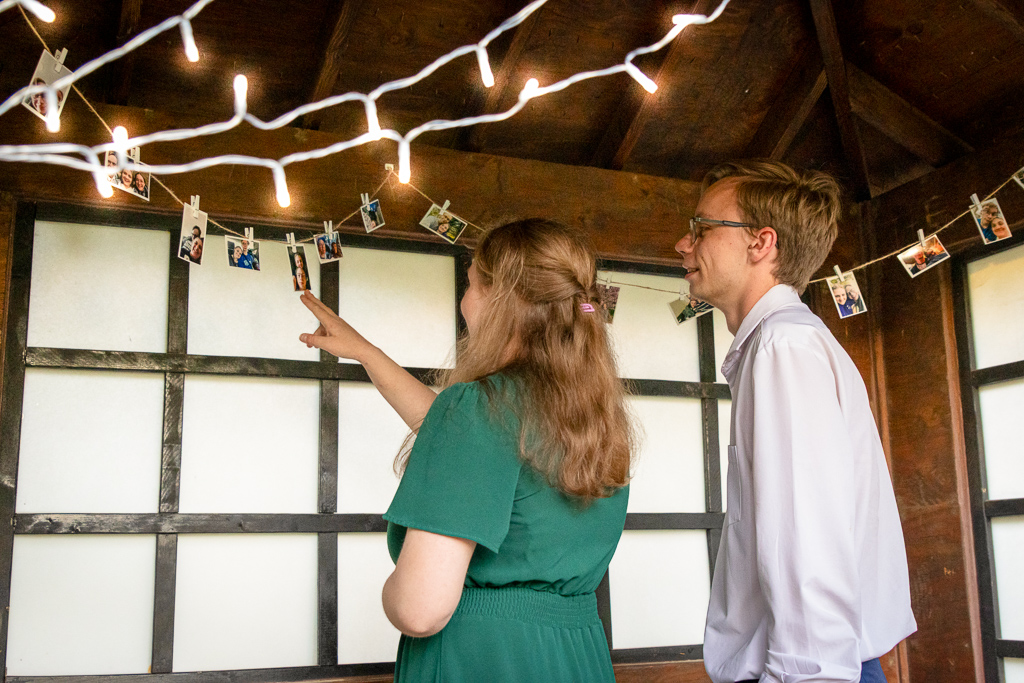 Brooke looking at photos hung by clips, Jon looking over her shoulder, under a shelter lit by fairy lights.