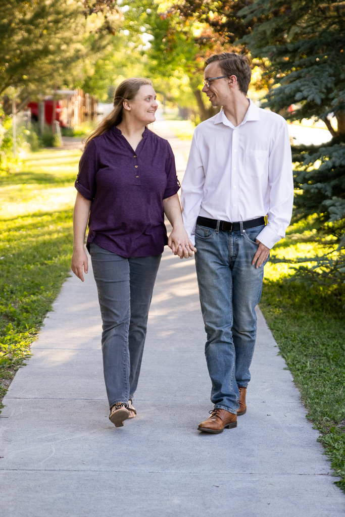 Brooke and Jon holding hands, walking down a sidewalk on a sunlit path.